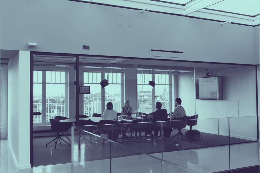 A group of four people having a meeting in a glass-walled conference room