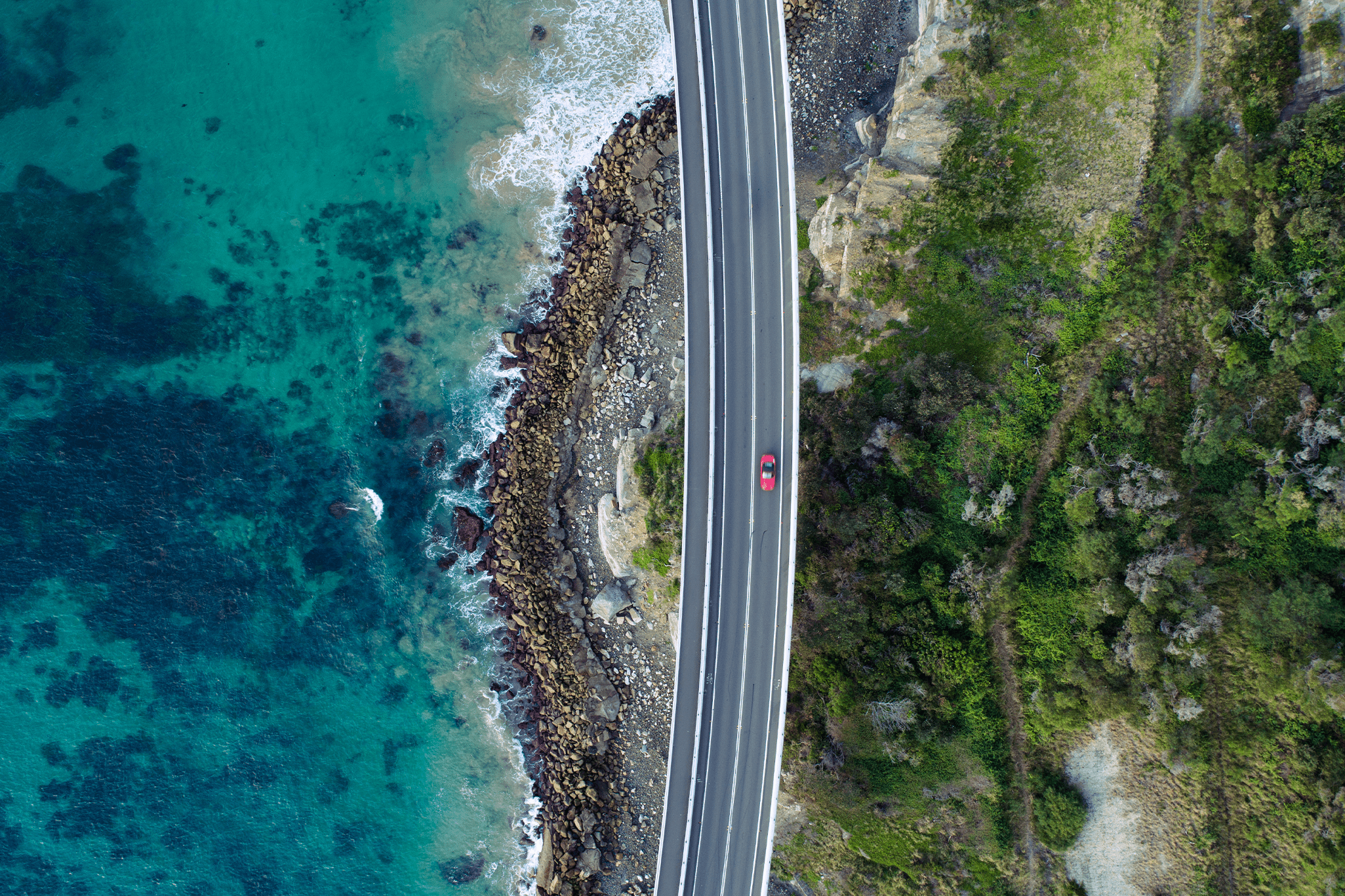 Aerial photo of a car driving through the cliff bridge